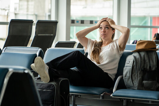 Mujer viajera sentada en sala de espera de un aeropuerto, tomandose la cabeza, impaciente y estresada por una gran demora en su pr&oacute;ximo vuelo