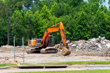 An orange and black backhoe is actively engaged at a construction site, clearing a pile of rubble...