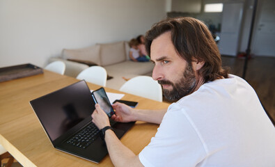 Man Teleworking from Minimalist Home with Laptop and Phone, Representing Remote Work and Digital...