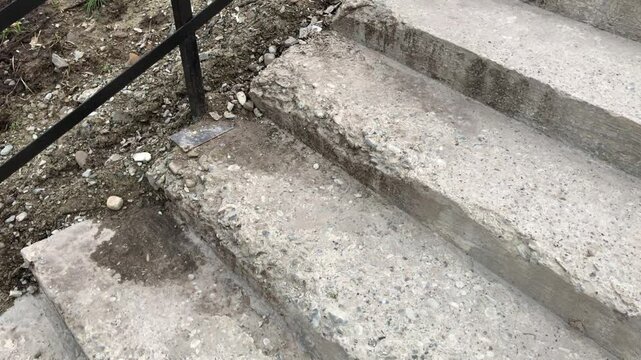 Damaged outdoor concrete stairs with crumbling edges and exposed aggregate near metal railing.