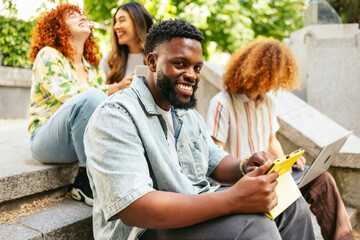 Obraz premium College student using tablet and laptop on campus steps with friends