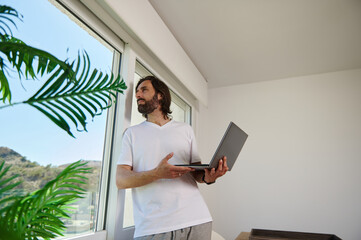 Relaxed Man Working From Home With Laptop, Facing Window
