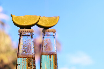 Beer with lime on blurred nature background. Bottled beer with lime, side view, free space. Alcoholic drink in a sealed bottle close-up. Drinks in summer
