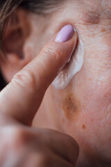 Fototapeta premium Close-up of an elderly woman face with moisturizer on her cheek