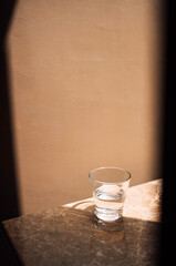 Close-up of a glass of clean water on a marble table. Transparent cup with water on a beige textured background.