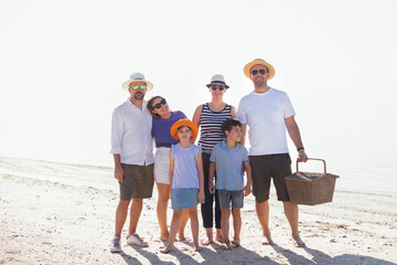A smiling group of friends posing and relaxing by the sea. Men and women and their children have a picnic together on the riverbank.