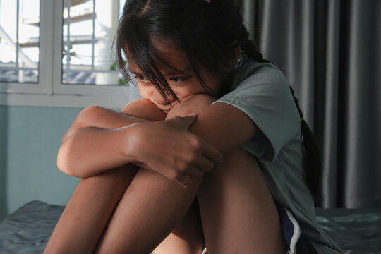 A sad asian child with lonely alone in a bedroom with natural sun light, Girl thinking about something, Childhood concept, Stress, mental health problems, depression and bullying in school ro social.
