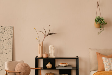 Minimalist composition of bedroom interior with bed, boucle armchair, round pouf, beige and orange bedding, plants, beige wall, vase with dried flowers and personal accessories. Home decor. Template.