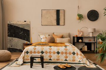 Interior design of bedroom interior with mock up poster frame, bed, orange bedding, wooden stool, black rack, pouf, plants, stylish lamp, sculpture and personal accessories. Home decor. Template.