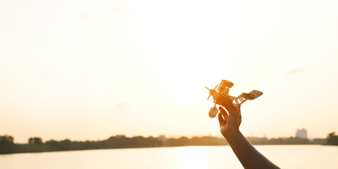 A person is holding a model airplane in the air. The airplane is yellow and has a propeller. The...
