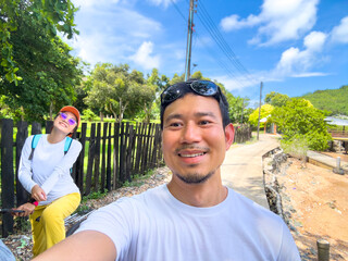 Asian man smiling selfie under blue sky and trees