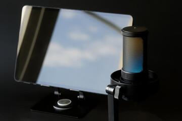 A sleek LED-lit condenser microphone paired with an electronic tablet on a dark desk, showcasing...