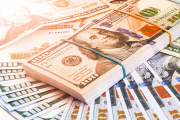 stack of hundred dollar bills tied with a rubber band with warm light