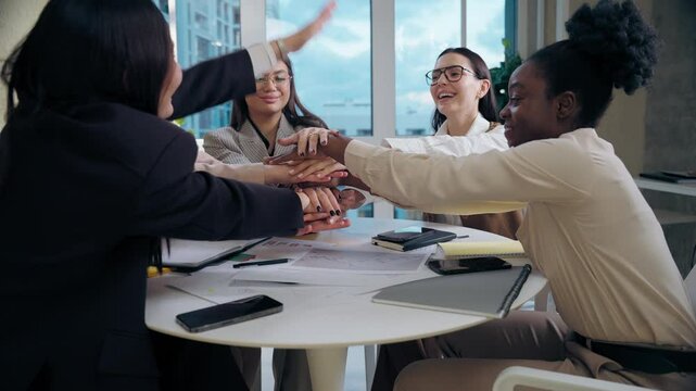 Happy multiethnic women females diversity team five girls group coworkers businesswomen business colleagues folding hands arms palms unity gesture cooperation success teamwork at office meeting table