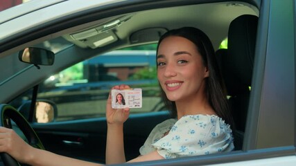 Happy smiling Caucasian joyful girl woman female driver sitting inside new car showing driving license at camera successfully passed test exam drive courses. Transportation test drive automobile rent