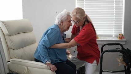 Fototapeta premium A elderly woman and her caregiver share a warm moment as they embrace helping her stand in a comfortable living room. Sunlight filters through the window.