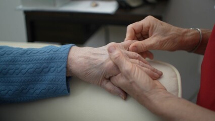 A caregivers hands gently massage the fingers and wrist of a patient to improve range of motion and comfort. This personal care takes place in a health clinic.