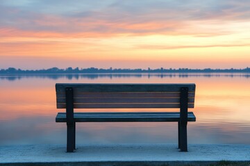 A lone park bench sits facing a calm lake under a breathtaking and vibrant sunrise painted across the sky.