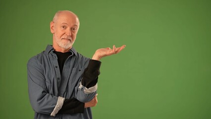 Mature man presents an expressive gesture with his hand while standing confidently in front of a solid green screen background, creating a perfect setup for announcements.