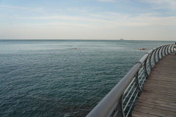 Fototapeta premium A peaceful boardwalk stretches along the calm sea, with endless blue water meeting the sky at the horizon.