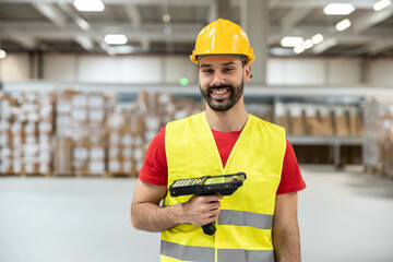Smiling male warehouse worker holding a barcode scanner in industrial storage environment.