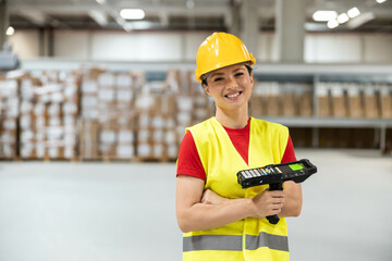 Female warehouse worker smiling while holding a barcode scanner in warehouse setting.