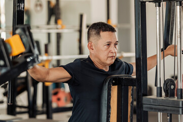 A focused middle-aged Southeast Asian man works on his posterior shoulders using a rear delt fly machine at an open-air gym.