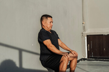 A focused middle-aged man performs a static wall sit against a concrete wall outside the gym in the...