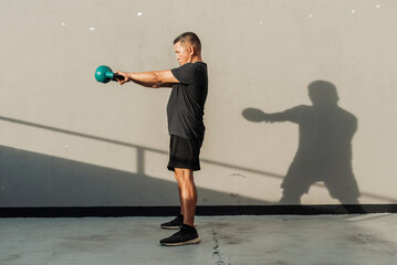 Side view - Middle-aged man swings kettlebell forward to shoulder height during outdoor functional training, emphasizing explosive strength and form control. Kettlebell swings exercise.