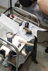 Tattoo artist creating a custom design for a young woman in a cozy Tbilisi studio. Details of the process, tattoo tools, ring light photography, and creative atmosphere
