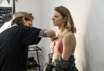 Tattoo artist creating a custom design for a young woman in a cozy Tbilisi studio. Details of the process, tattoo tools, ring light photography, and creative atmosphere