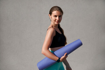 Young woman in athletic wear holding a yoga mat, showcasing fitness lifestyle and wellness, with a...