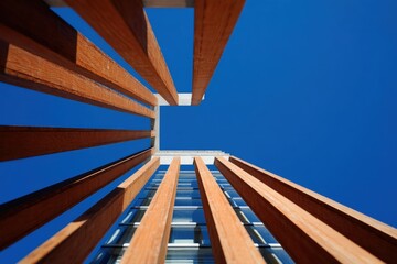 sustainable building materials,A modern building facade with vertical wooden slats shot from a low angle against a clear blue sky.