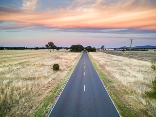 A country road leads of into the distance under a bank of coloured clouds