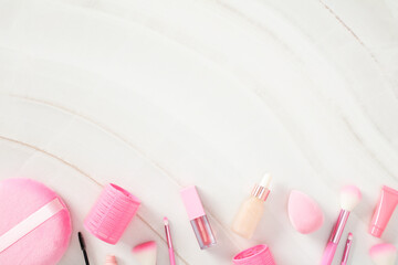 Pink decorative cosmetics and makeup brushes on white marble background.