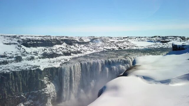 Stock video of the famous Dettifoss waterfall in Iceland. Dettifoss is Icelands biggest waterfall, and the most powerful in all of Europe. The land around the waterfall is covered in snow. It is a sun