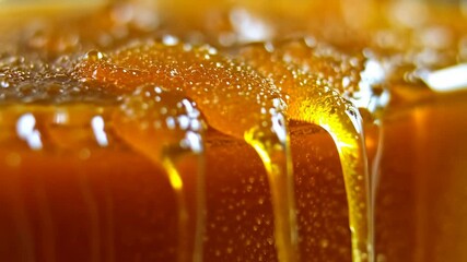 Close up shot of honey dripping from glass with a yellow hue and bubbles creating a sweet looking treat.