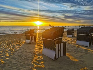Zinnowitz, Mecklenburg-Vorpommern, Deutschland: Ein malerischer Sonnenaufgang taucht den menschenleeren Strand in goldenes Licht. Strandkörbe stehen ruhig im Sand, die Szene strahlt Freiheit, Ruhe und