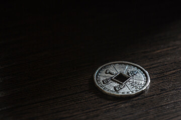 Dilong metal coin. The coin is round with a square hole in the middle and decorative patterns. The coin's gray metal and dark brown table.