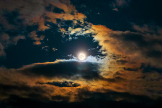 Full moon surrounded by colorful glowing clouds in beautiful night sky