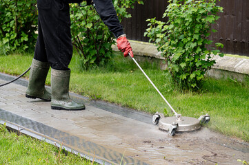 Cleaning a paved pathway with a pressure washer on a sunny day in a green garden. Professional paving stone cleaning.