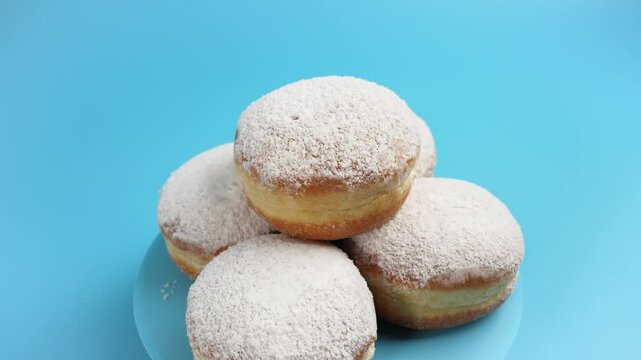 Sweet Berliner buns with powdered sugar on top rotate on a blue background. The buns are stacked on top of each other.