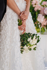 without a face. The bride is holding a delicate beautiful bouquet in her hands. 