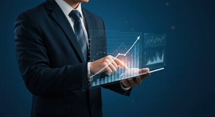 Businessman uses a tablet displaying rising graph data against a dark blue background.