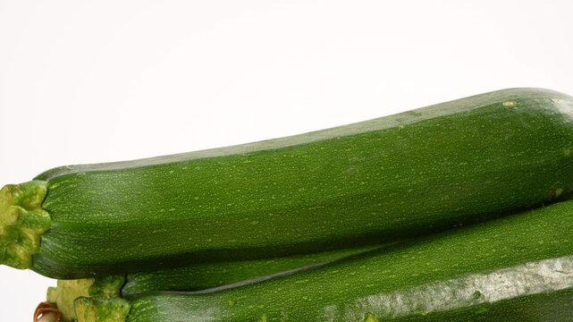 Three green zucchini are stacked on top of each other. The zucchini are fresh and ready to be eaten