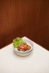 Indonesian Spicy Beef Matah, Fresh Lettuce Garnish Accompanying Savory Meat Dish on a Minimalistic Table Setting in a Modern Restaurant