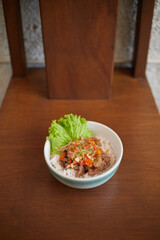 Indonesian Spicy Beef Matah, Bowl of Rice Topped With Savory Meat and Fresh Vegetables on a Wooden Table