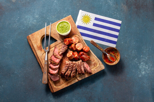 Celebrate Uruguay independence day with traditional asado featuring grilled meat, sausage, and sauce alongside the national flag - Powered by Adobe