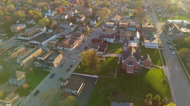 Drone video flying over New Glarus Wisconsin at sunset showing city buildings, rooftops, and the Swiss United Church of Christ in golden light.
