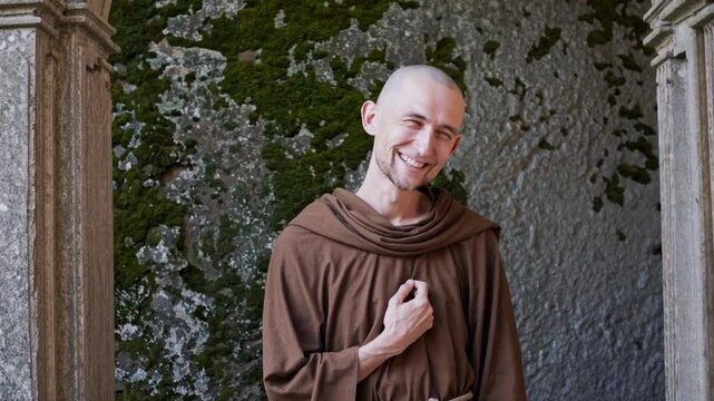 Moine souriant en robe de bure devant un mur ancien, sc&egrave;ne joyeuse et spirituelle en ext&eacute;rieur

